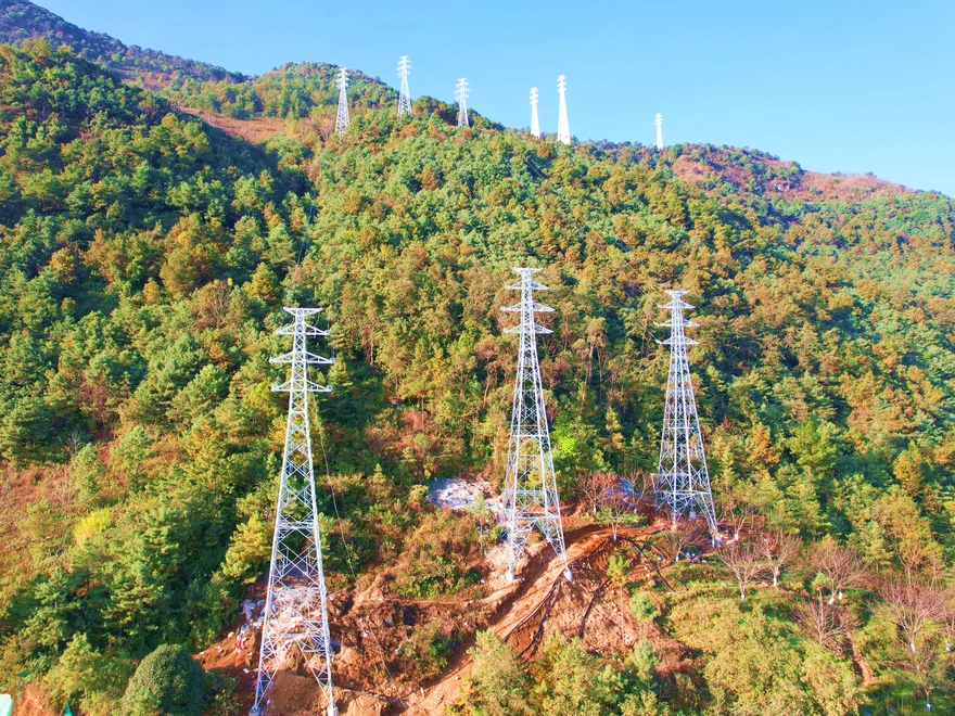 Overhead transmission line towers stretching across forested mountain ridges